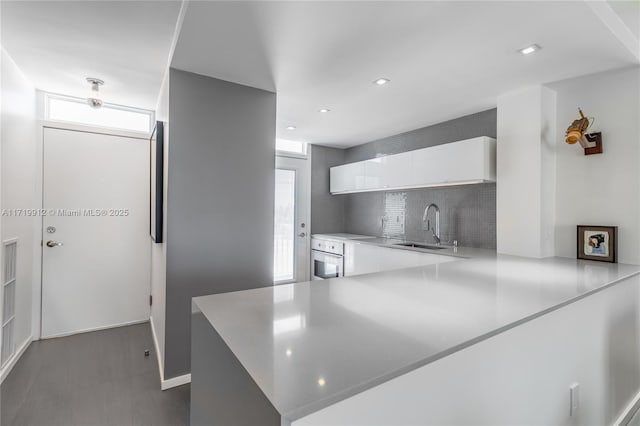 kitchen with sink, white cabinets, white oven, kitchen peninsula, and decorative backsplash