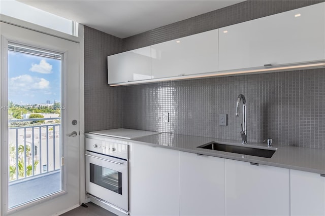 kitchen with sink, white cabinetry, backsplash, and oven