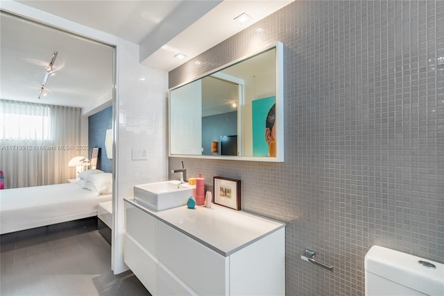 bathroom featuring tile walls, track lighting, vanity, and toilet