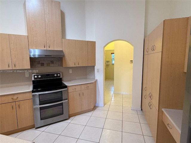 kitchen featuring light brown cabinetry, a towering ceiling, stainless steel range with electric cooktop, and light tile patterned flooring