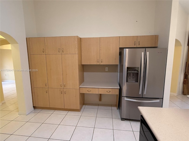 kitchen featuring a towering ceiling, stainless steel fridge, light brown cabinets, and light tile patterned floors