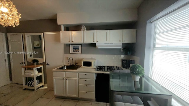 kitchen with tasteful backsplash, a sink, light tile patterned floors, white microwave, and under cabinet range hood