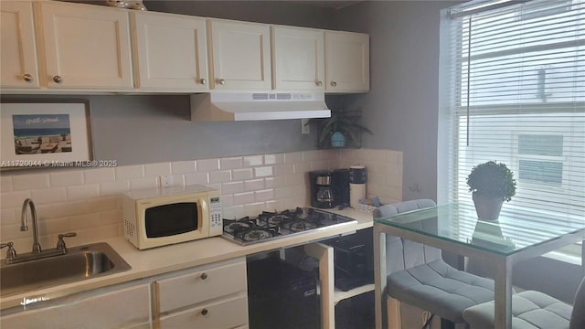 kitchen with under cabinet range hood, backsplash, light countertops, a sink, and white microwave