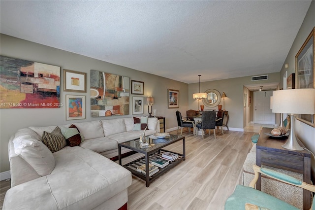 living room featuring a notable chandelier, light hardwood / wood-style floors, and a textured ceiling