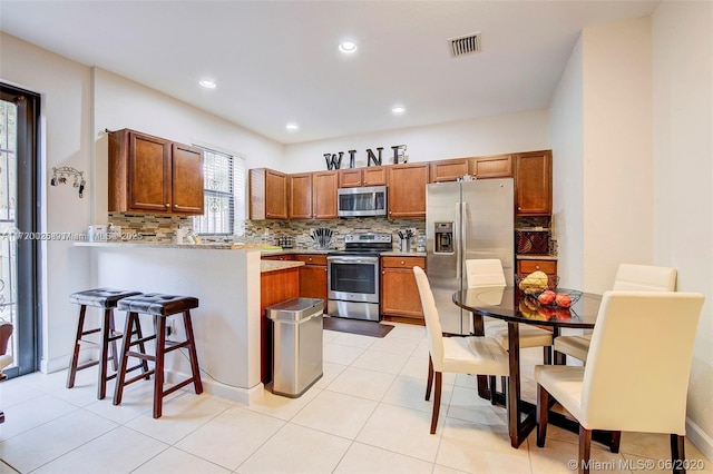 kitchen with decorative backsplash, appliances with stainless steel finishes, kitchen peninsula, a breakfast bar, and light tile patterned flooring