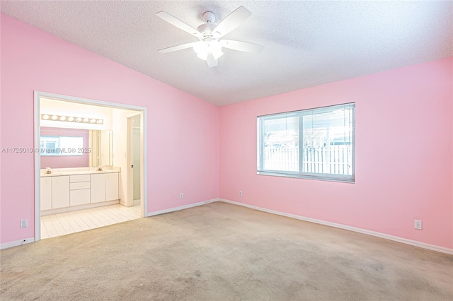 unfurnished bedroom with ensuite bathroom, ceiling fan, light colored carpet, and vaulted ceiling