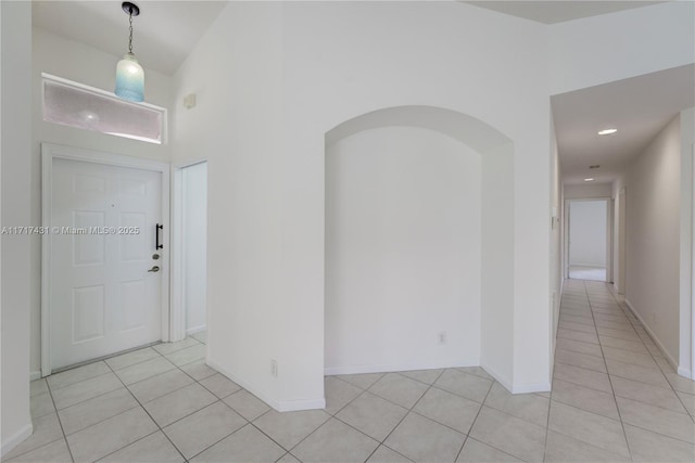 foyer with a towering ceiling, light tile patterned floors, baseboards, and arched walkways