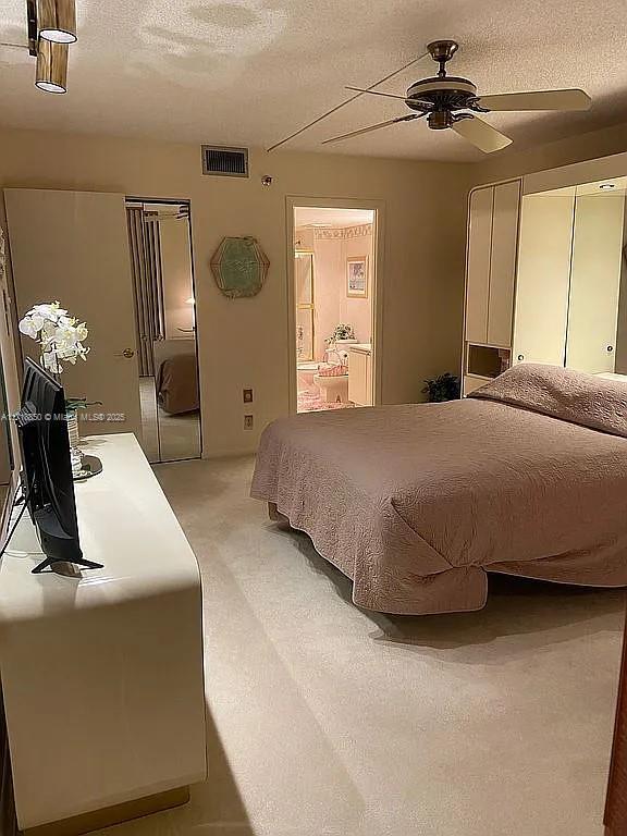 bedroom with ceiling fan, ensuite bathroom, and a textured ceiling