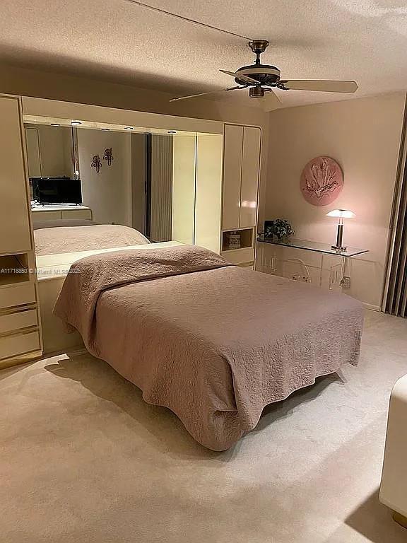 carpeted bedroom with ceiling fan and a textured ceiling