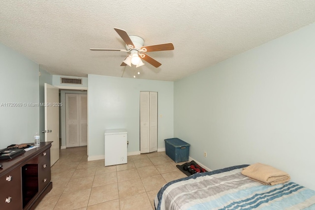 bedroom featuring ceiling fan, light tile patterned floors, and a textured ceiling