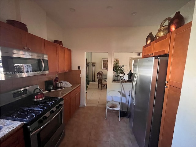 kitchen with tile patterned flooring, light stone countertops, stainless steel appliances, and tasteful backsplash