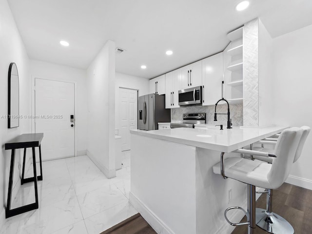 kitchen with white cabinets, decorative backsplash, appliances with stainless steel finishes, a kitchen bar, and kitchen peninsula