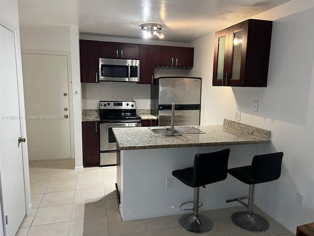 kitchen featuring kitchen peninsula, sink, appliances with stainless steel finishes, a kitchen breakfast bar, and light tile patterned floors