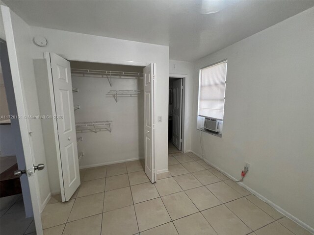 unfurnished bedroom featuring cooling unit, a closet, and light tile patterned flooring