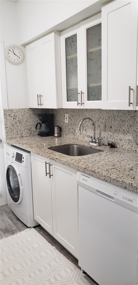 kitchen with dishwasher, tasteful backsplash, washer / dryer, white cabinets, and sink