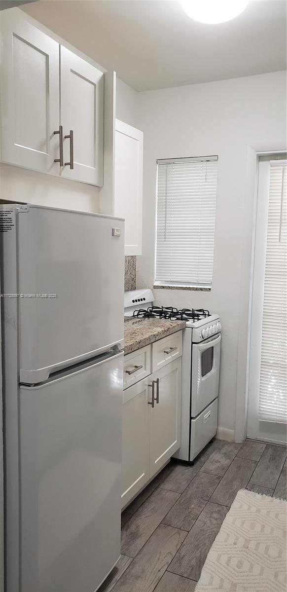 kitchen with stainless steel refrigerator, white gas range oven, light stone counters, and white cabinetry