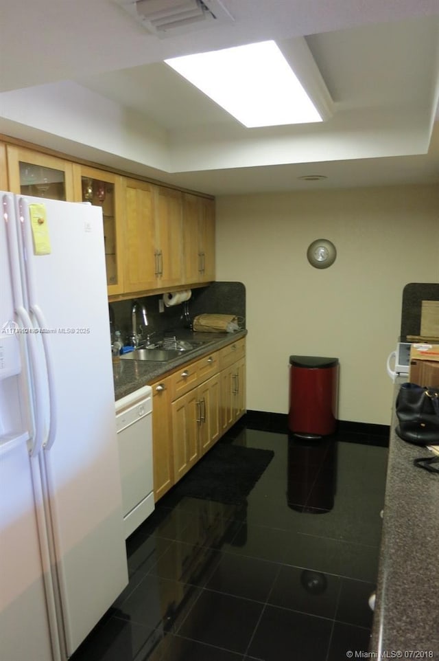 kitchen featuring sink, dark tile patterned floors, white appliances, a tray ceiling, and light brown cabinetry