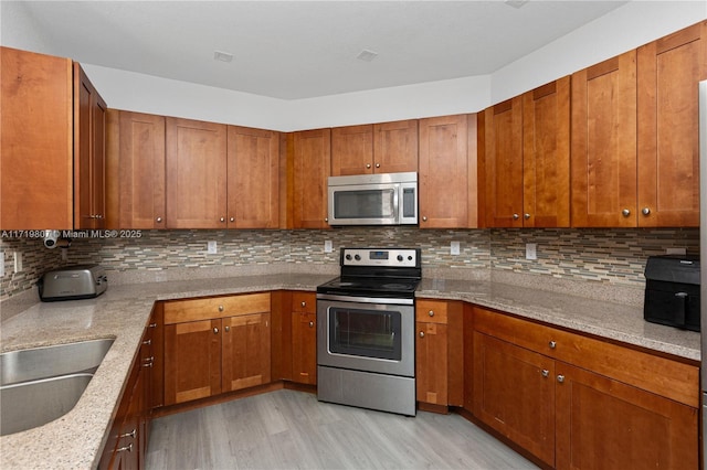 kitchen featuring light stone countertops, appliances with stainless steel finishes, decorative backsplash, sink, and light hardwood / wood-style flooring