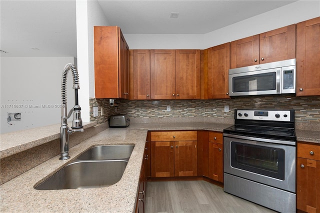 kitchen featuring decorative backsplash, light stone counters, light wood-type flooring, and appliances with stainless steel finishes