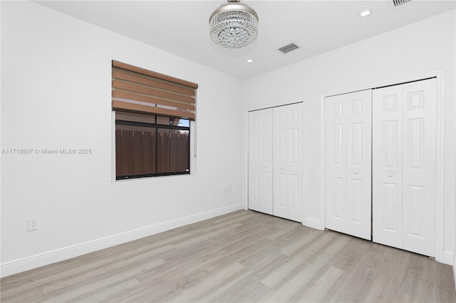 unfurnished bedroom with light wood-type flooring, two closets, and an inviting chandelier