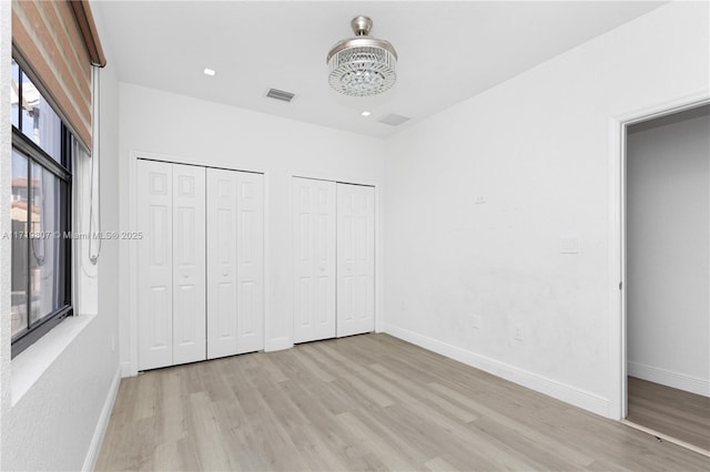 unfurnished bedroom featuring light wood-type flooring, two closets, an inviting chandelier, and multiple windows