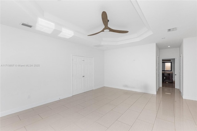 unfurnished room featuring ceiling fan, light tile patterned flooring, and a tray ceiling