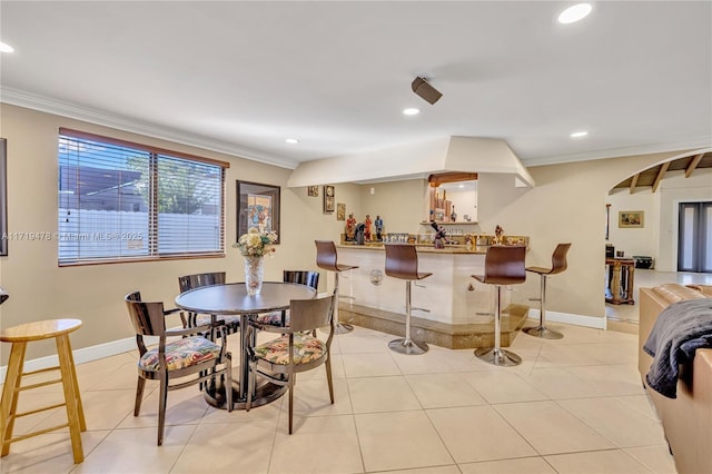 dining space with light tile patterned flooring, ornamental molding, and bar area