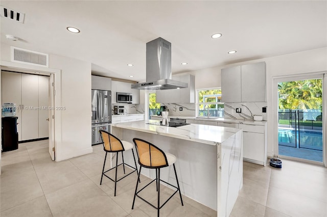 kitchen featuring a breakfast bar area, island range hood, a center island, stainless steel appliances, and decorative backsplash