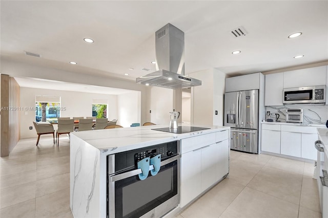 kitchen featuring appliances with stainless steel finishes, light stone counters, wall chimney range hood, white cabinets, and a kitchen island