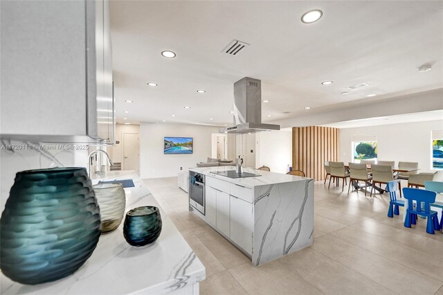 kitchen featuring island range hood, black electric cooktop, a large island with sink, white cabinetry, and oven