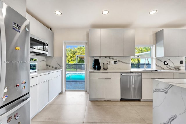 kitchen featuring sink, appliances with stainless steel finishes, white cabinetry, light stone countertops, and decorative backsplash