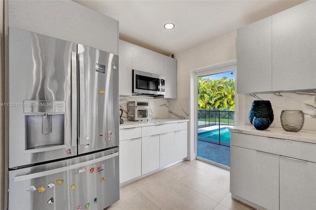 kitchen with backsplash, light tile patterned flooring, white cabinets, and stainless steel appliances