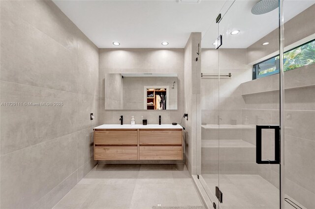 bathroom with vanity, a shower with door, and tile walls