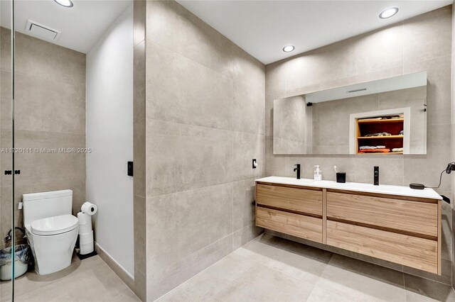 bathroom featuring tile patterned floors, vanity, tile walls, and toilet