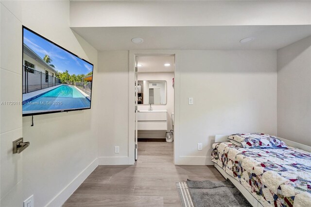 bedroom with connected bathroom, light hardwood / wood-style floors, and sink