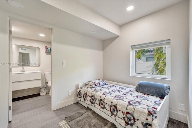 bedroom featuring light wood-type flooring, ensuite bath, and sink