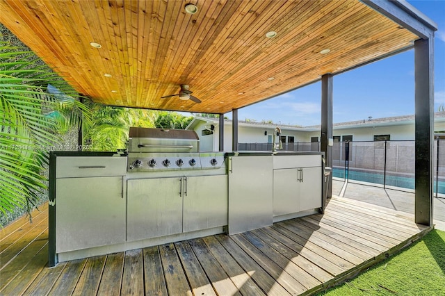 wooden terrace featuring exterior kitchen, ceiling fan, a grill, and a fenced in pool