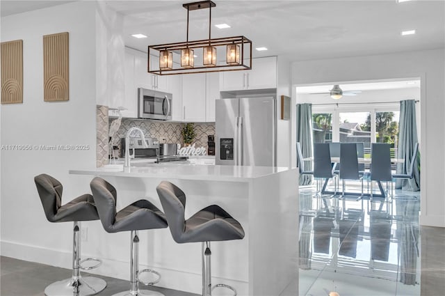 kitchen featuring a breakfast bar, hanging light fixtures, kitchen peninsula, appliances with stainless steel finishes, and white cabinetry