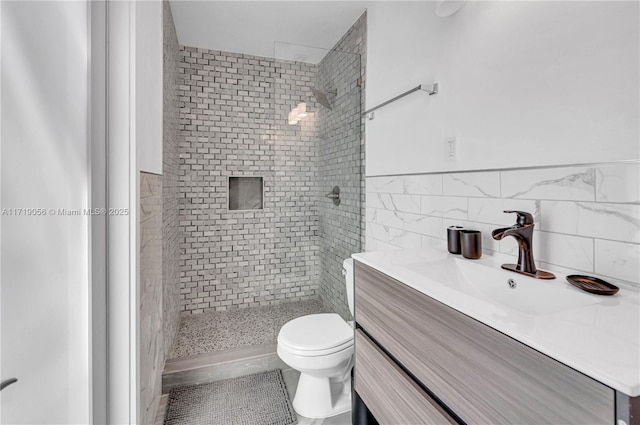 bathroom with tile patterned floors, a tile shower, vanity, tile walls, and toilet