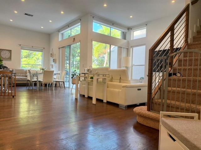 living room with dark wood-type flooring, visible vents, stairway, and a towering ceiling