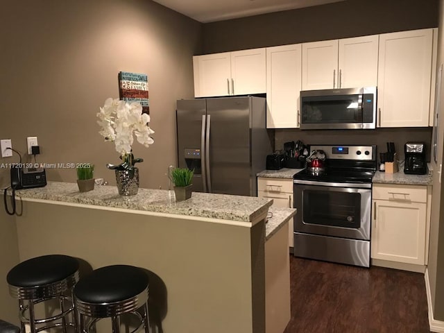 kitchen featuring light stone countertops, appliances with stainless steel finishes, a breakfast bar, and white cabinetry