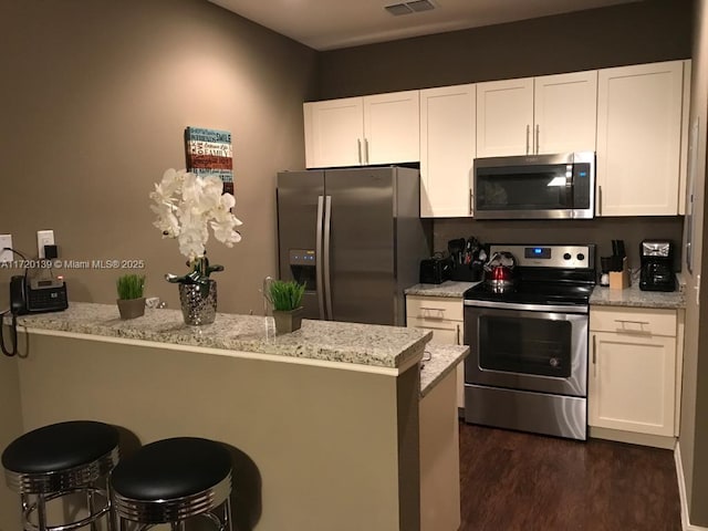 kitchen with light stone counters, stainless steel appliances, dark hardwood / wood-style floors, white cabinetry, and a breakfast bar area