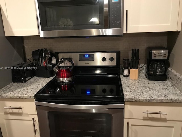 kitchen with backsplash, light stone counters, white cabinets, and stainless steel appliances