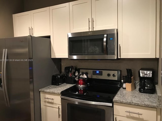 kitchen with stainless steel appliances, white cabinetry, tasteful backsplash, and light stone counters