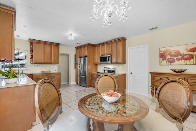 kitchen with appliances with stainless steel finishes, light stone counters, decorative light fixtures, a chandelier, and light tile patterned flooring