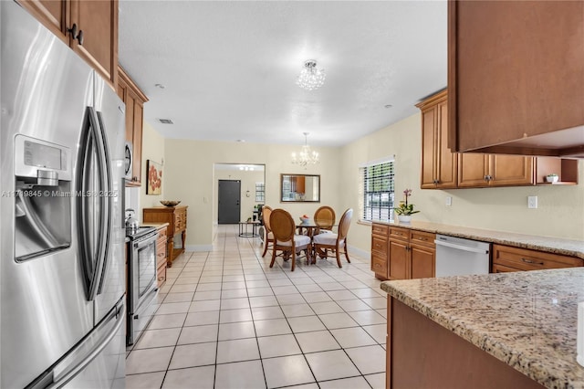 kitchen with light stone countertops, pendant lighting, a chandelier, light tile patterned flooring, and appliances with stainless steel finishes