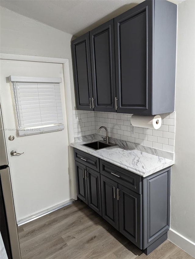 kitchen featuring decorative backsplash, light wood-type flooring, light stone counters, and sink