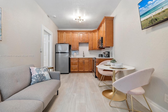 kitchen with tasteful backsplash, a textured ceiling, stainless steel appliances, sink, and light hardwood / wood-style flooring