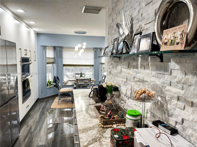 kitchen with light stone countertops, a textured ceiling, an inviting chandelier, white cabinetry, and hanging light fixtures