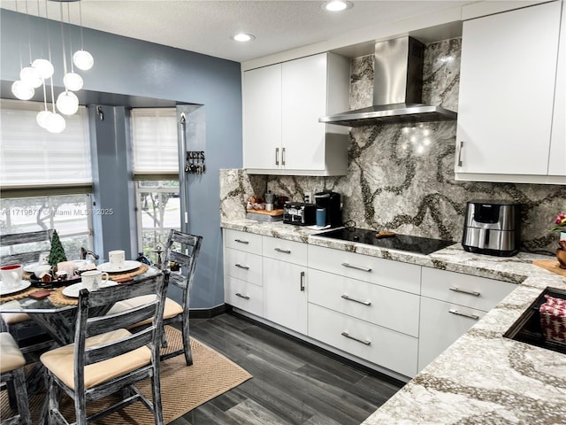 kitchen featuring black electric stovetop, light stone counters, wall chimney exhaust hood, pendant lighting, and white cabinetry